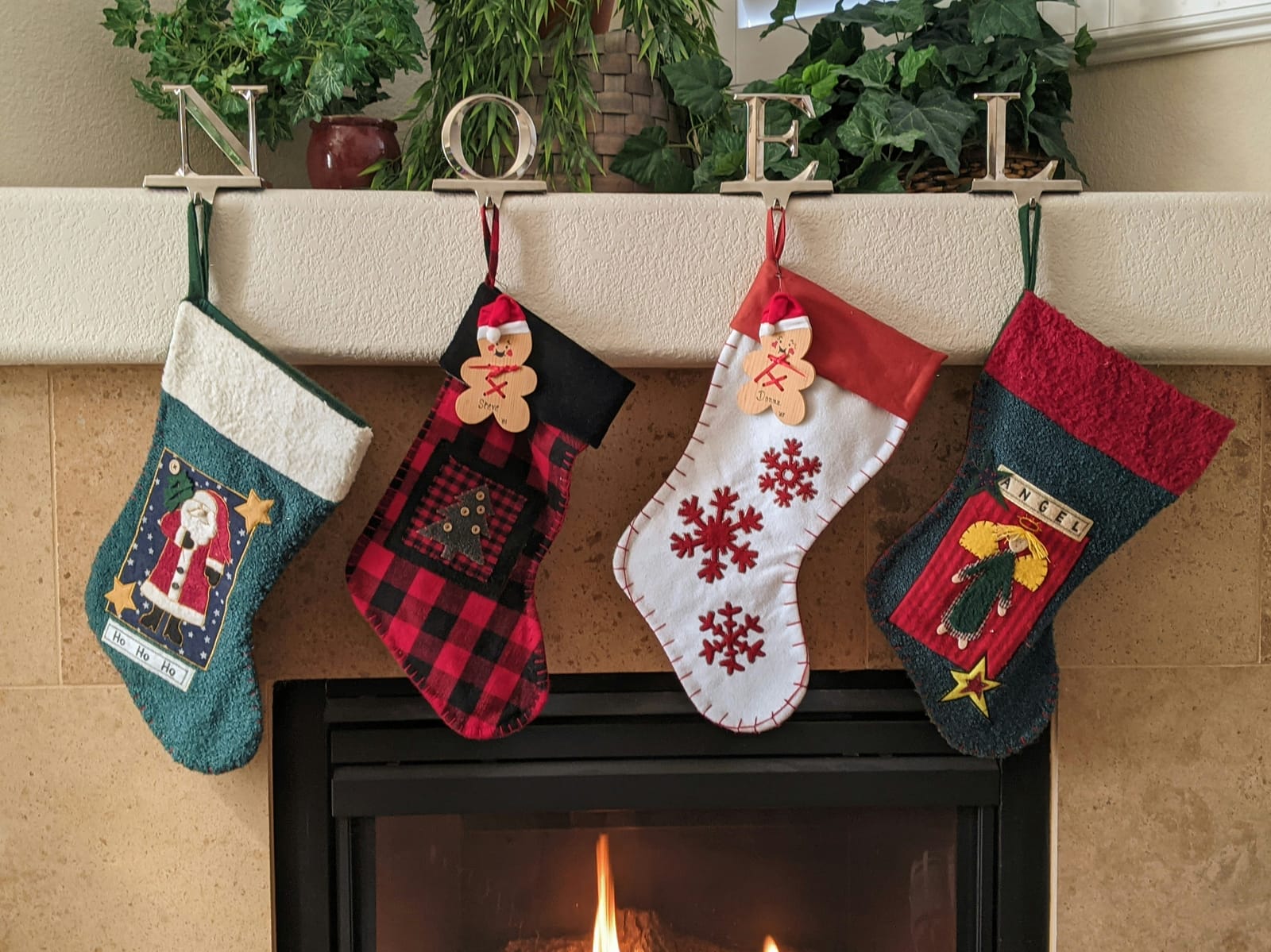 Four handmade Christmas stockings hanging from NOEL stocking holders on a mantel above a lit fireplace